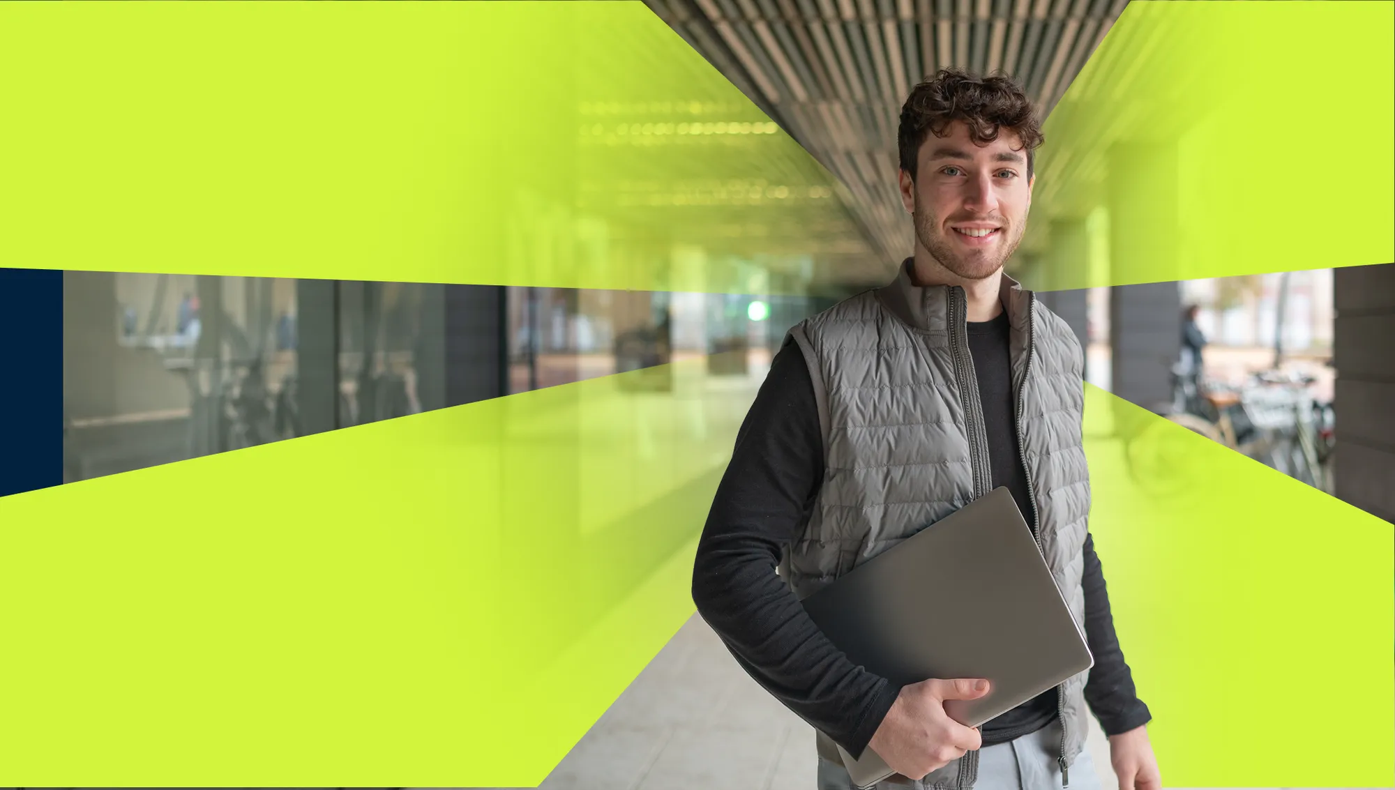 home Lachende jonge man die met een laptop in zijn handen staat in een lichte kantooromgeving